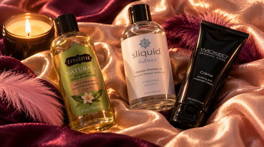 Massage oil bottles and a pheromone gift set with candle arranged on dusty-rose silk satin with pink feathers, dried rose petals, and warm candlelight