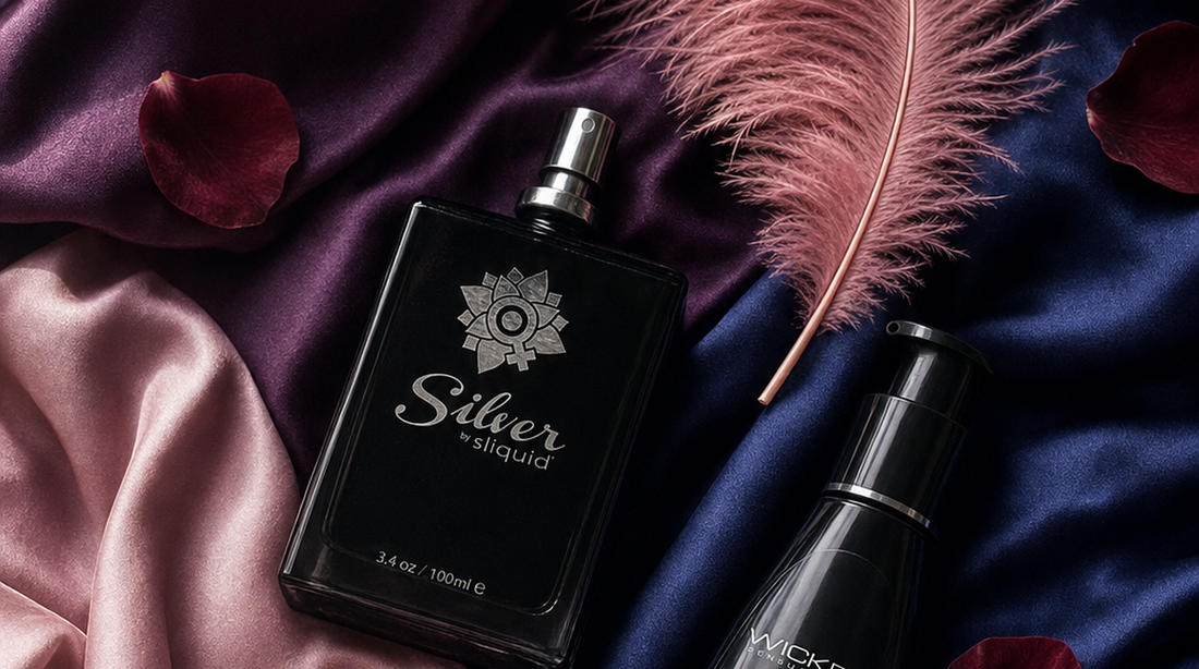 Editorial flat-lay featuring Sliquid Silver and Wicked Sensual Care Hybrid lubricant bottles, purple silk, pink feather, rose petals