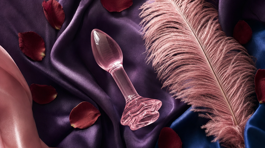 Editorial flat-lay featuring b-Vibe training plugs and glass rose butt plug on purple silk with pink feather