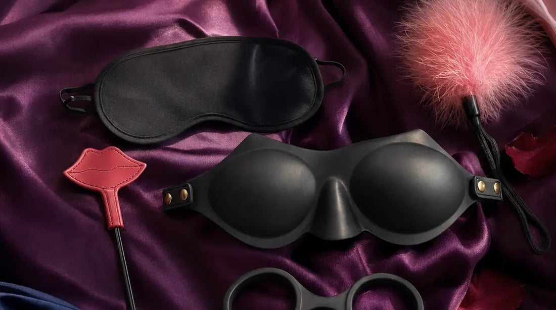 Editorial flat-lay featuring Blush Temptasia Ardor Blindfold and Sex & Mischief Kiss Kit on purple silk with pink feather and rose petals