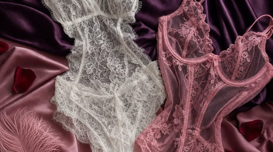 Editorial flat-lay featuring white eyelash lace romper and pink lace mesh teddy, purple silk, pink feather, rose petals