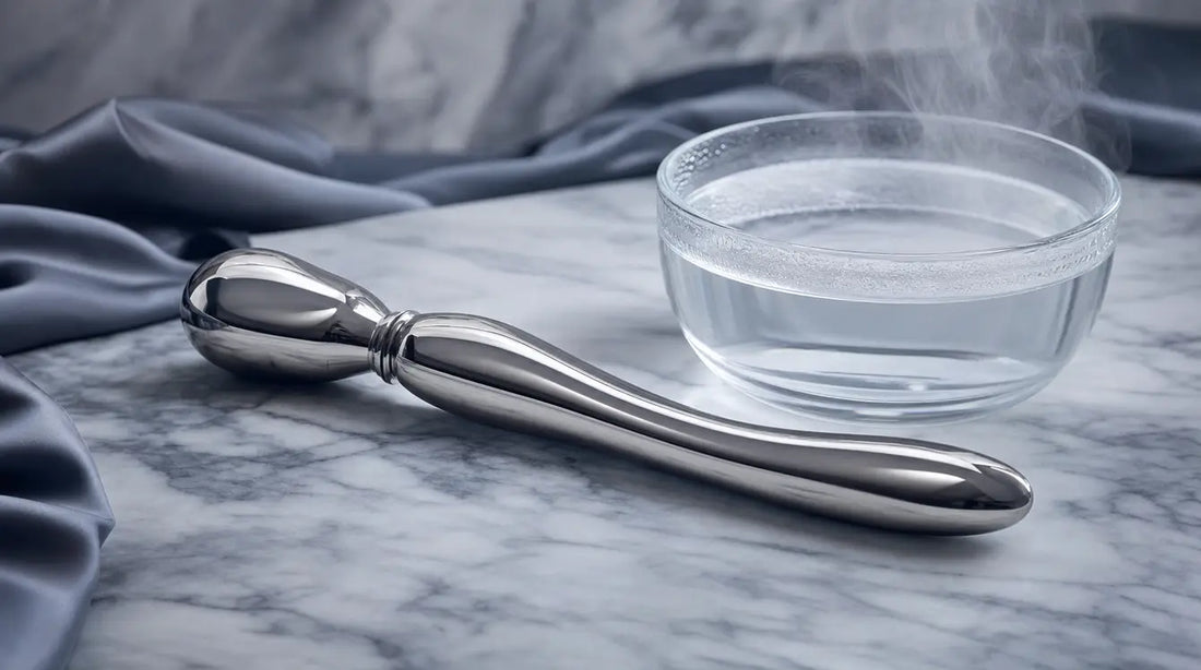 Polished stainless steel wand resting on marble with a warm water bowl — temperature play and weighted prostate toy guide banner