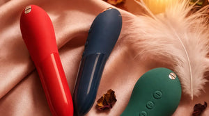 We-Vibe Tango X Cherry, Tango X Midnight Blue, and Touch X Green Velvet on blush pink silk satin with feathers and candlelight