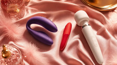 We-Vibe Chorus couples vibrator, Tango X bullet, and Wand 2 on blush pink silk with feathers — brand comparison hero image