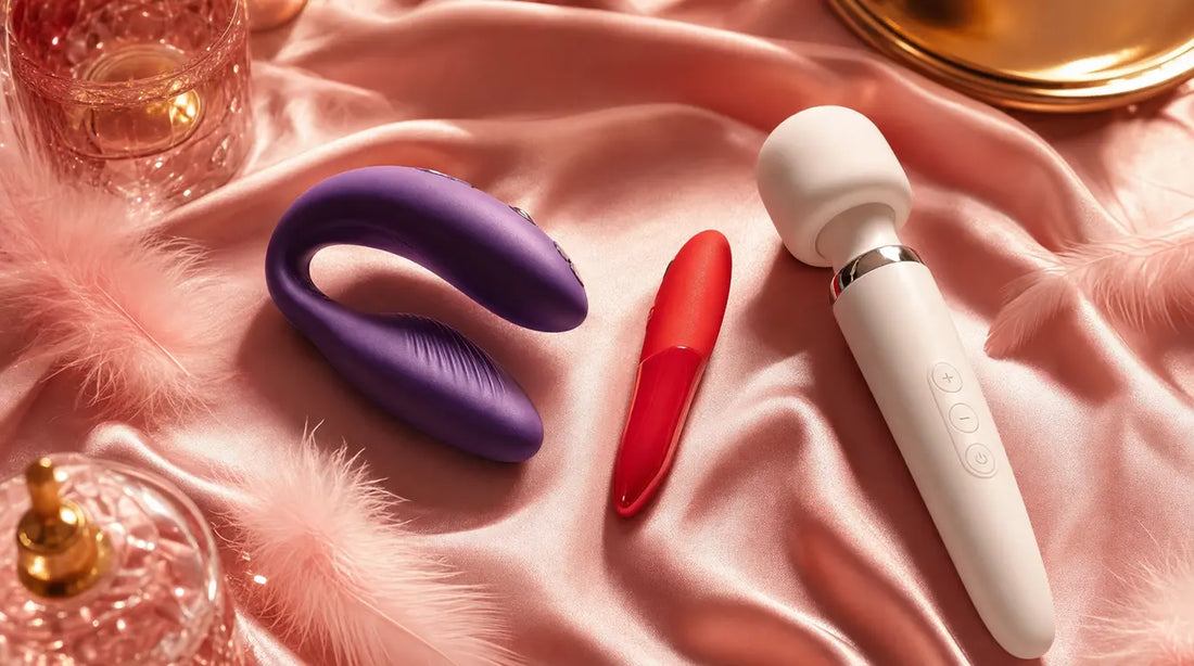We-Vibe Chorus couples vibrator, Tango X bullet, and Wand 2 on blush pink silk with feathers — brand comparison hero image
