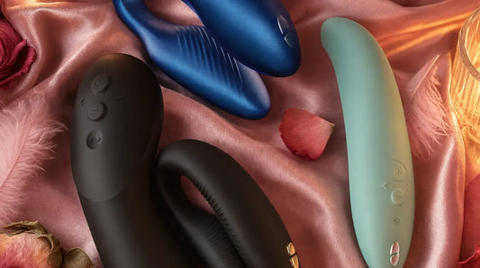 We-Vibe Chorus, Chorus Pro, and Melt 2 arranged on blush pink silk with pink feathers, rose petals, and candlelight