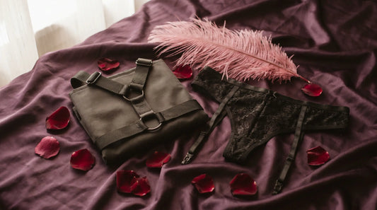 Editorial flat-lay of strap-on harnesses on aubergine silk with pink feather