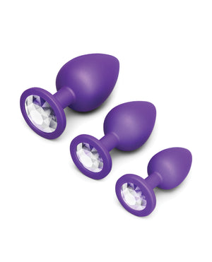 Set of three purple anal plugs with crystal-like centers on a white background