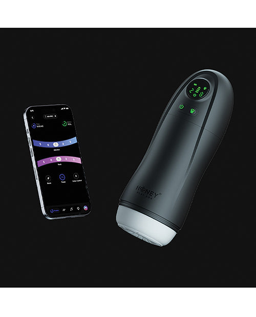 Honey Play Box Kai Pro masturbator in black with its sleeve opening visible, shown beside a smartphone running the control app