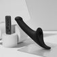 Strap-On-Me Multi Orgasm Vibrating Dildo in black shown upright with its remote control in a styled studio setting, no packaging shown