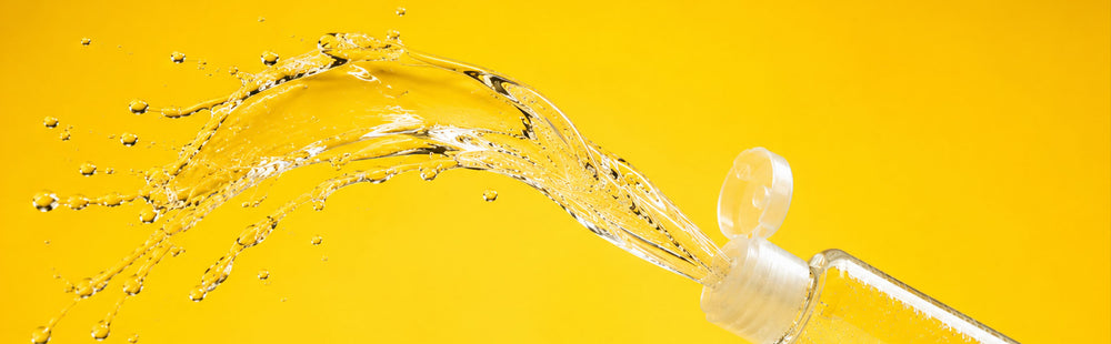 Bottle of oil lubricant poured with a splash against a yellow background